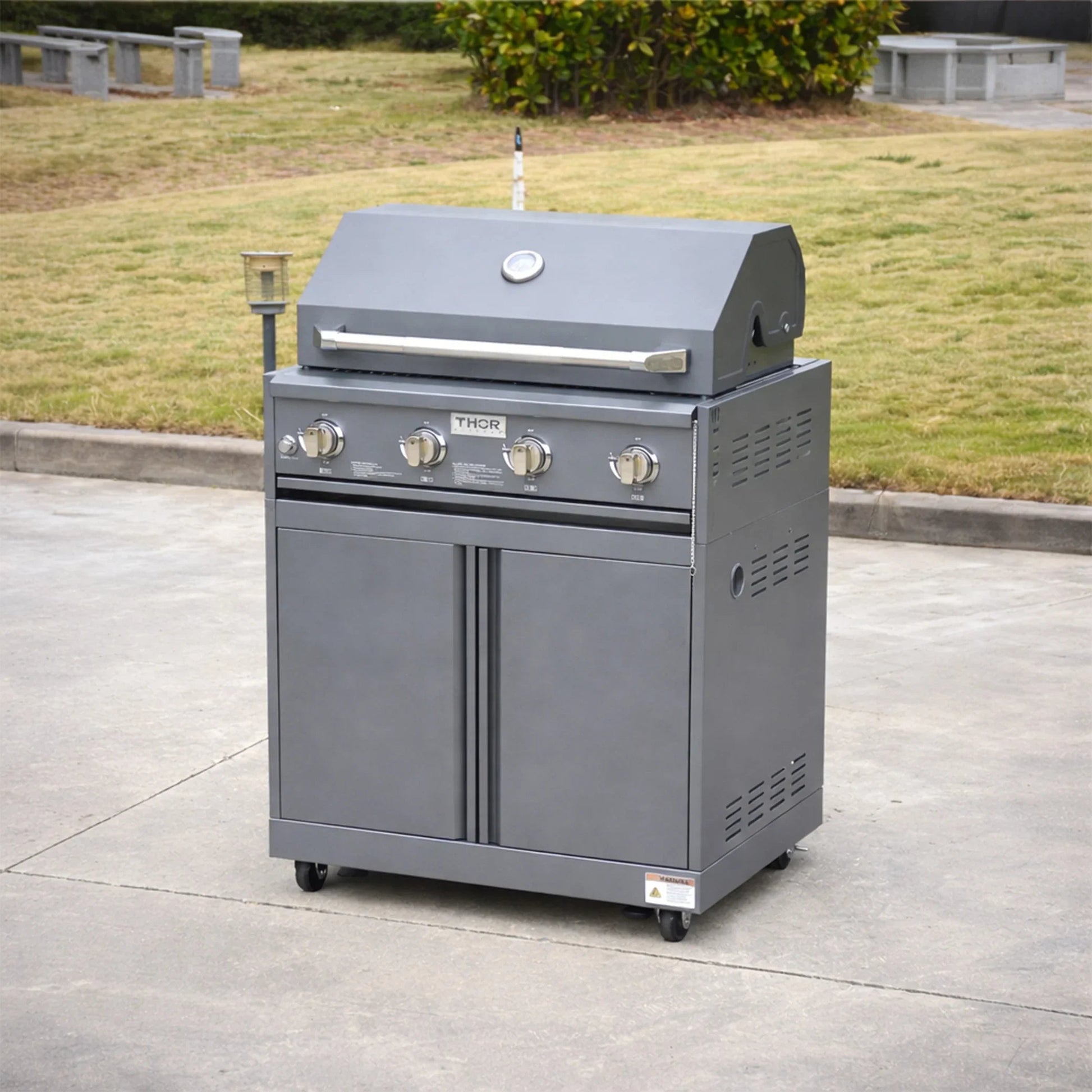 Stainless steel outdoor gas grill with four burners and storage cabinets on wheels in a garden