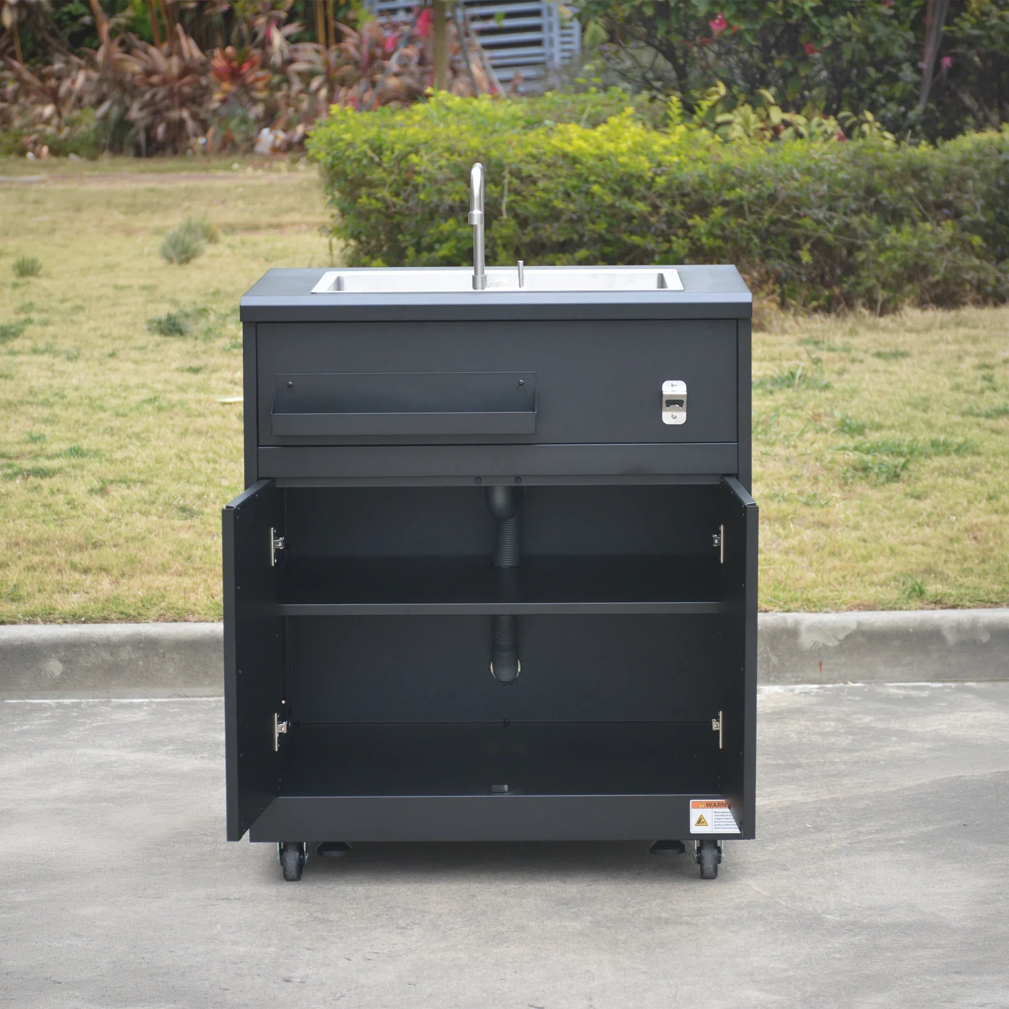 Outdoor black metal sink cabinet with open storage doors, faucet, and wheels on concrete