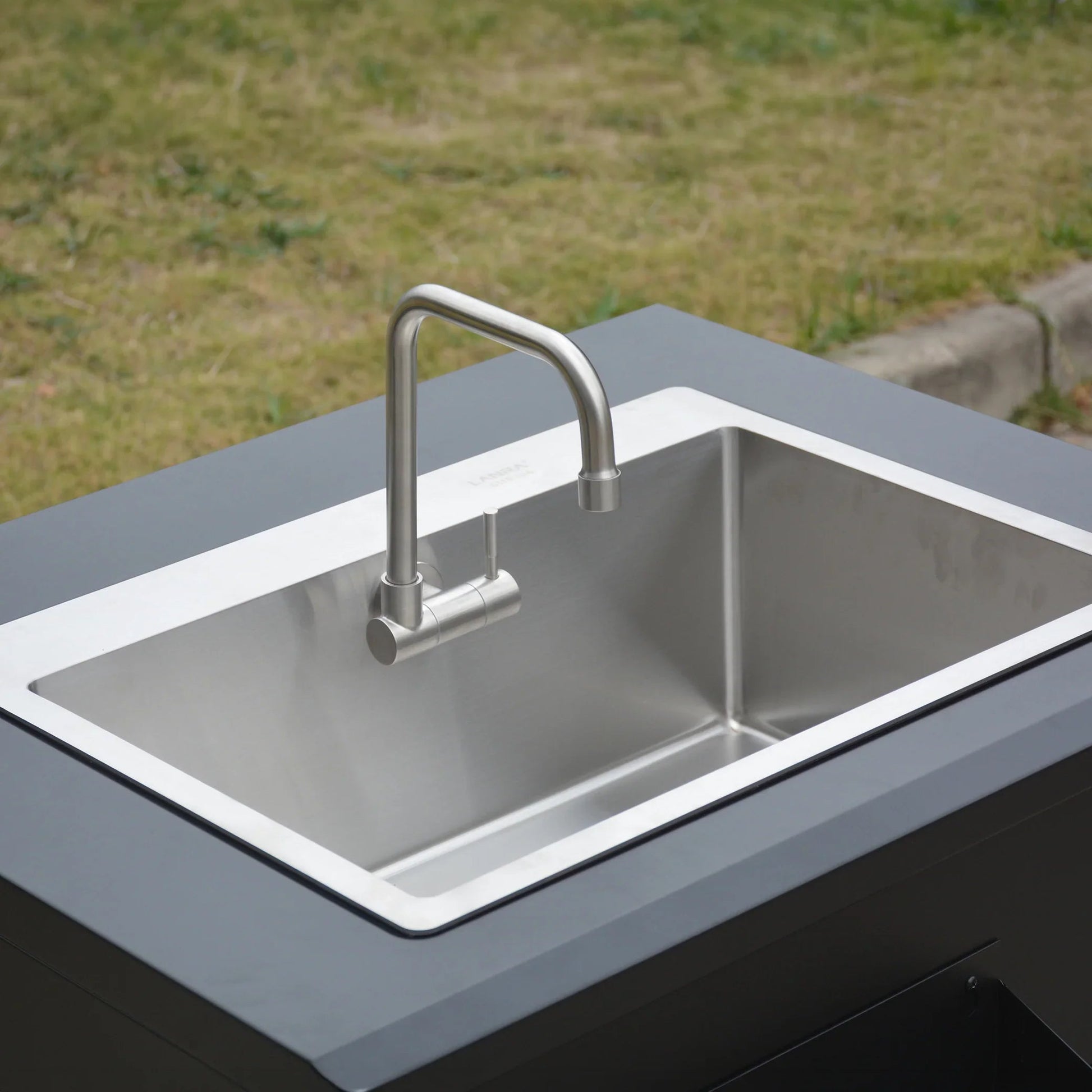 Stainless steel kitchen sink with modern faucet installed in outdoor countertop