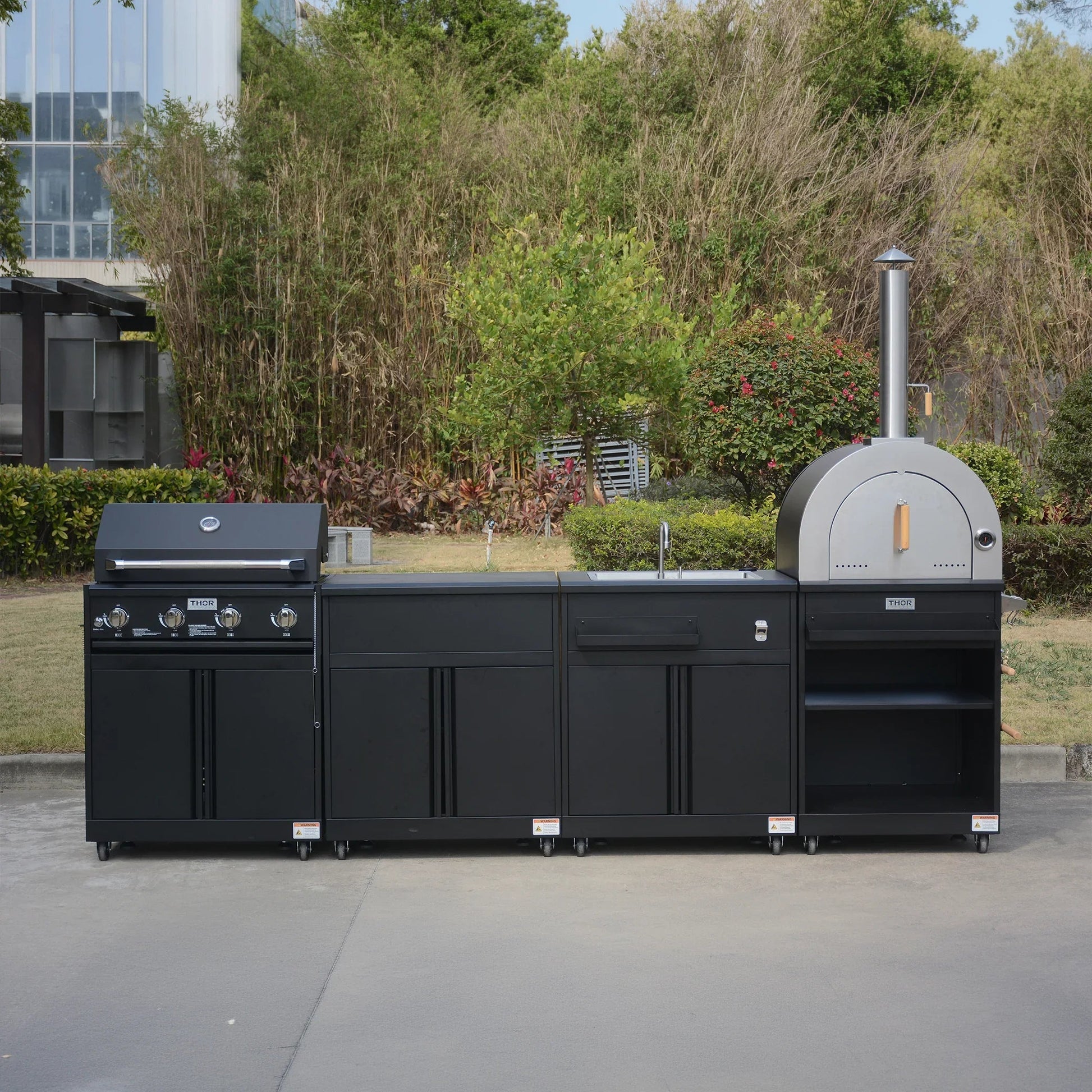 Outdoor modular kitchen with black cabinets, built-in grill, oven, and sink on patio