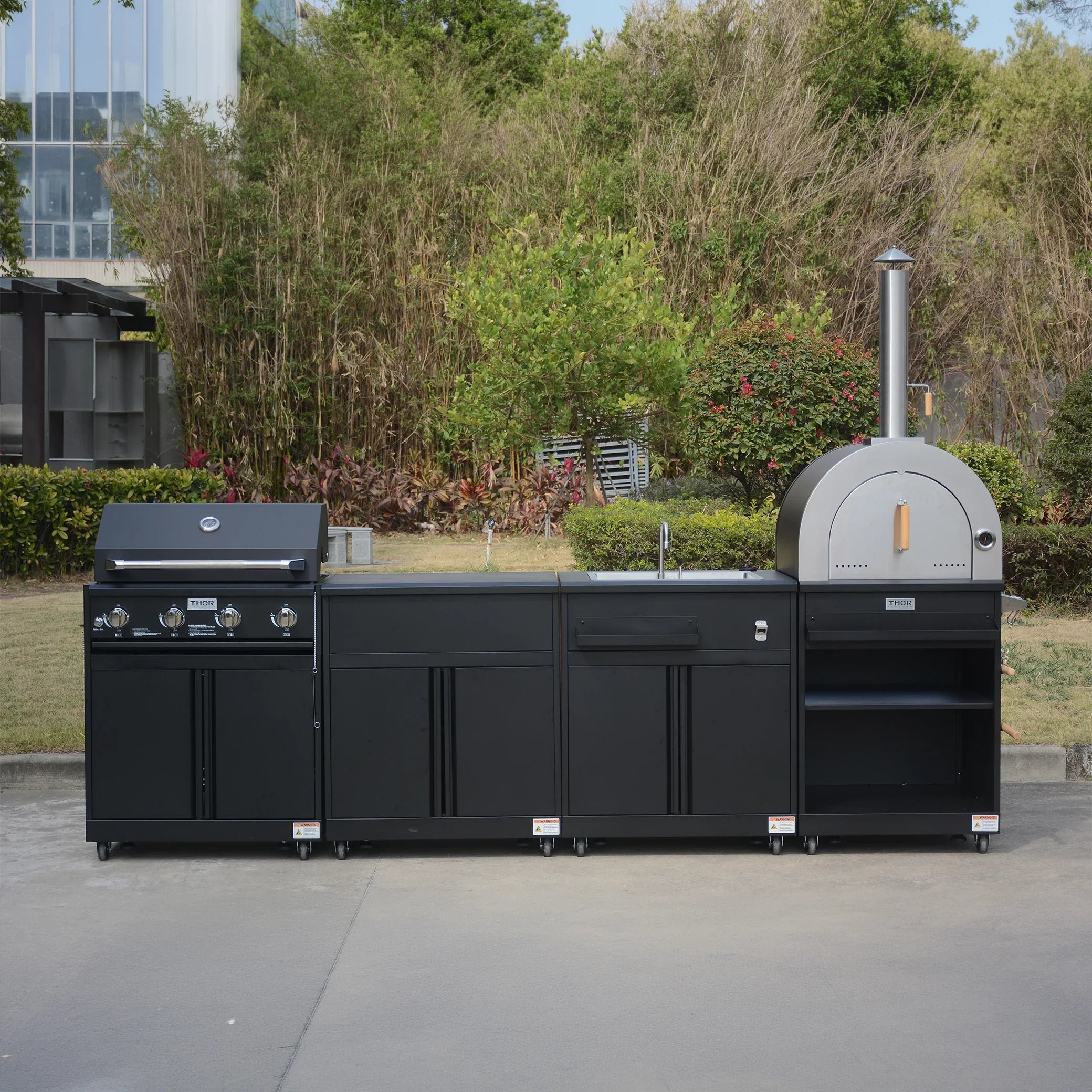 Outdoor modular kitchen with black cabinets, built-in grill, oven, and sink on patio