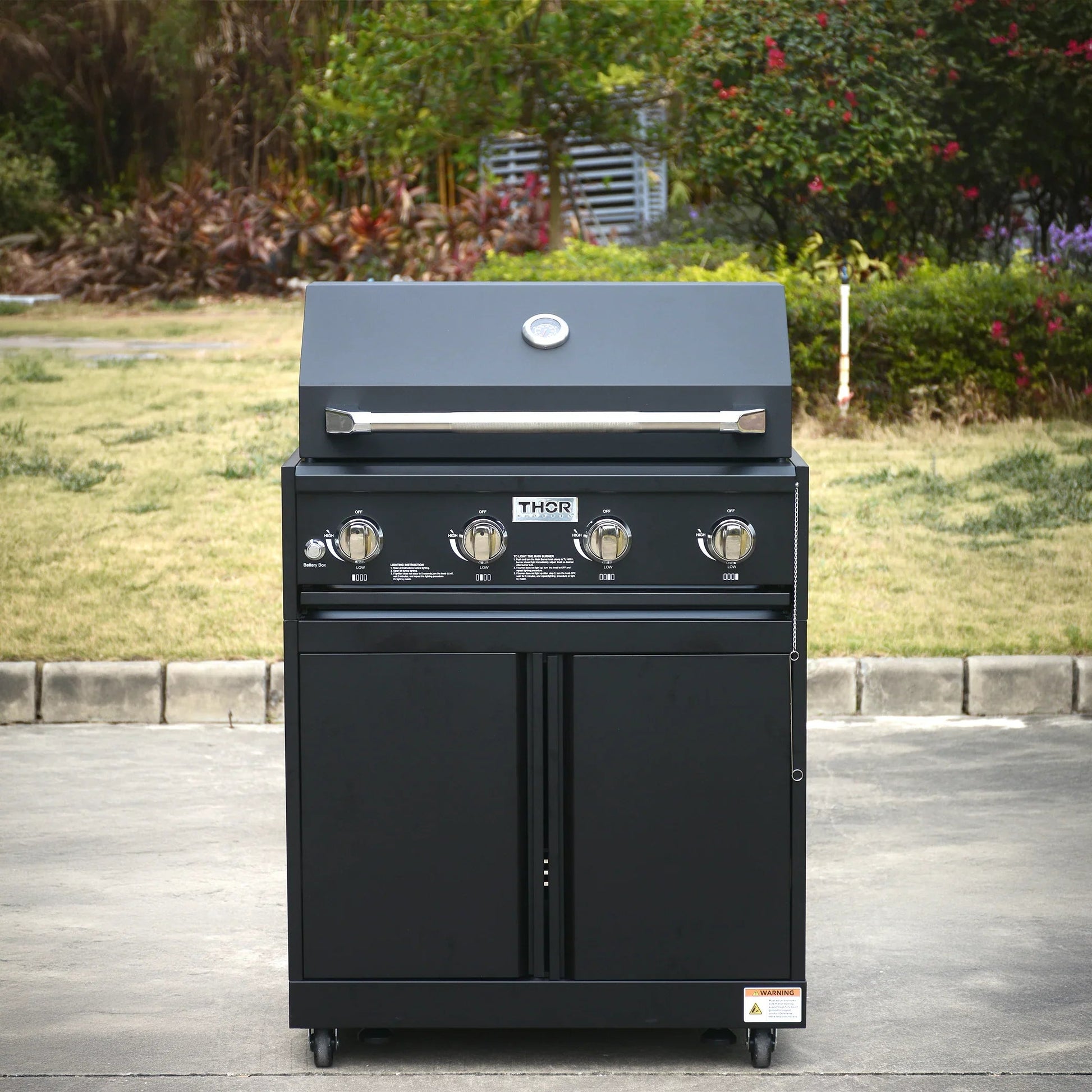 Black outdoor gas barbecue grill with four control knobs on patio, garden background