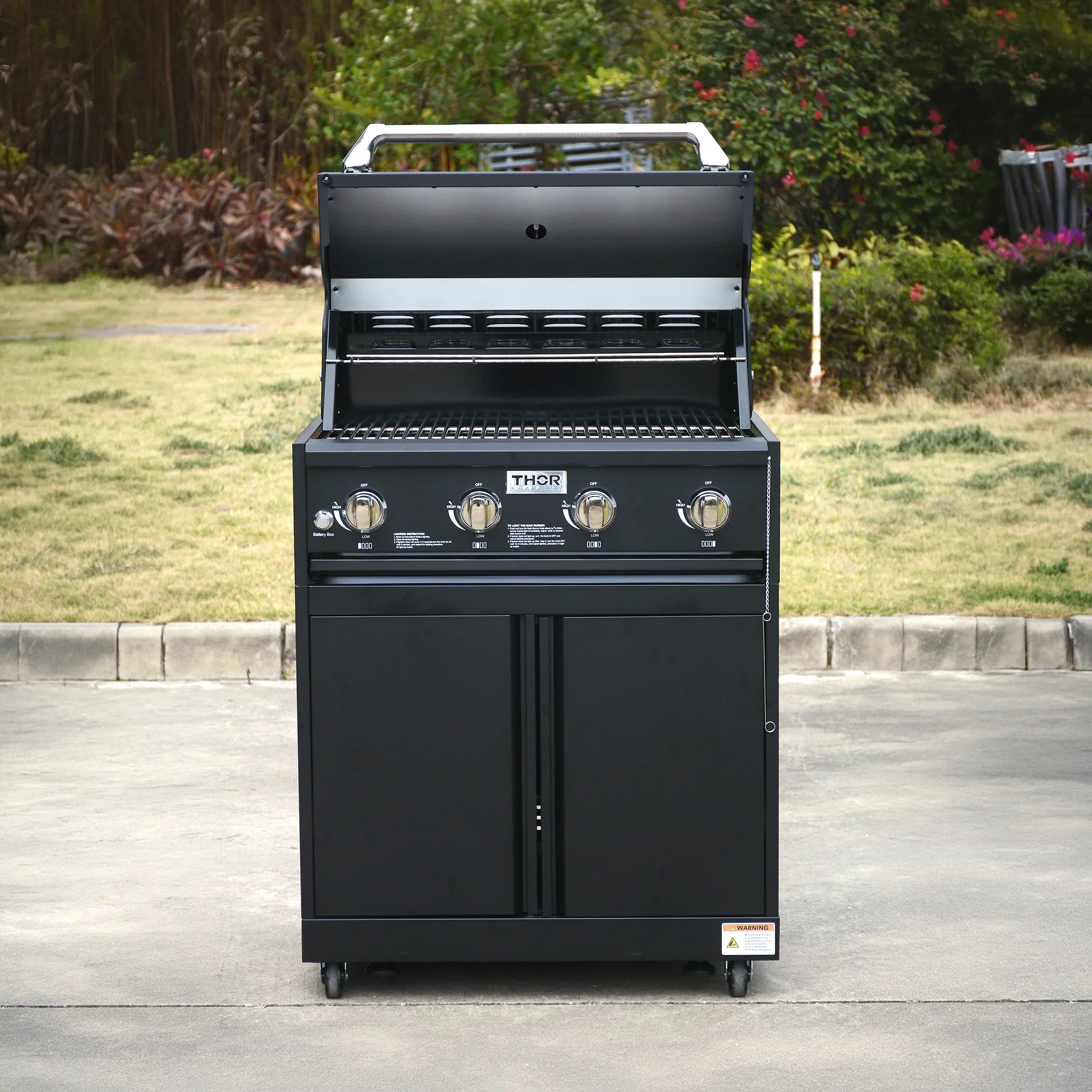 Outdoor black gas grill with four burners and open lid on a patio in a garden setting