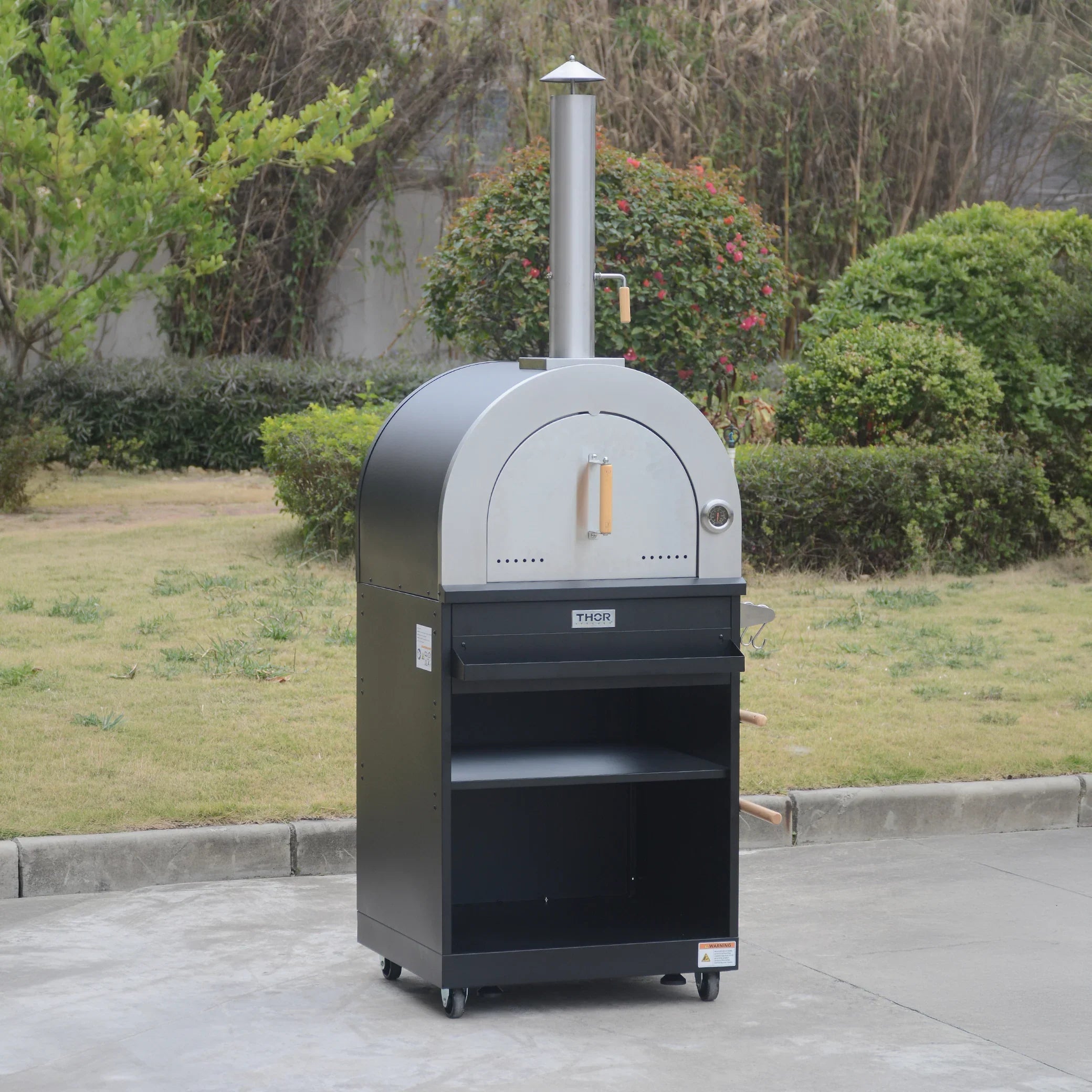 Outdoor wood-fired pizza oven with chimney, stainless steel door, and storage shelves on wheels